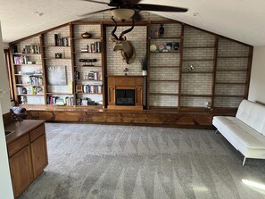 Un salon de style industriel, avec une cheminée, des étagères à livres, une tête de cerf fixée au mur et un ventilateur de plafond.