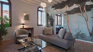 Una sala de estar moderna con sofá, sillón, una mesa de centro de vidrio y un mural con árboles.