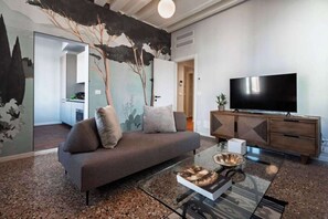 En moderne stue med sofa, glasbord, fladskærms-tv og et træskab.