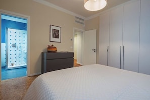 Une chambre à coucher comprenant un lit, une commode, une armoire et une porte donnant accès à une salle de bain.