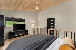 A bedroom with a bed, a TV, a fireplace, a balcony, and a ceiling fan.