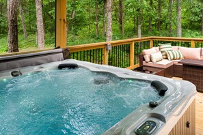 A hot tub on a wooden deck with a view of a forest.