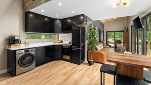 Cozinha moderna com armários pretos, máquina de lavar embutida e área de refeições com mesa e cadeiras de madeira.