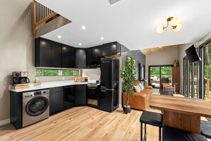A modern kitchen with black cabinetry, a built-in washing machine, and a dining area with a wooden table and chairs.