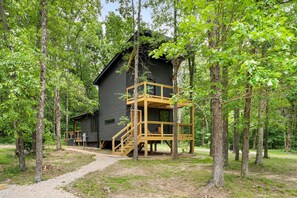 A cabin with a wooden deck and stairs, surrounded by trees.
