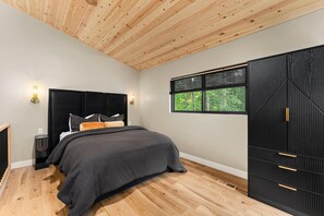 A bedroom with a bed, a nightstand, a wardrobe, a window with a view, and a wooden ceiling.
