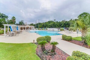 Ein Schwimmbecken mit Liegestühlen, einer überdachten Terrasse und einem kleinen Gebäude mit Dach.