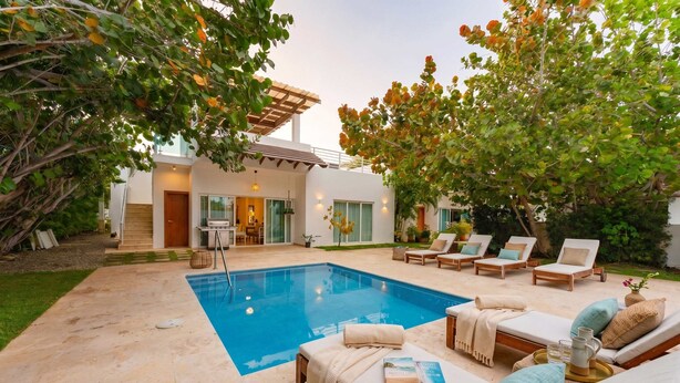 Une maison moderne dotée d’une piscine, de chaises longues et d’un patio couvert.