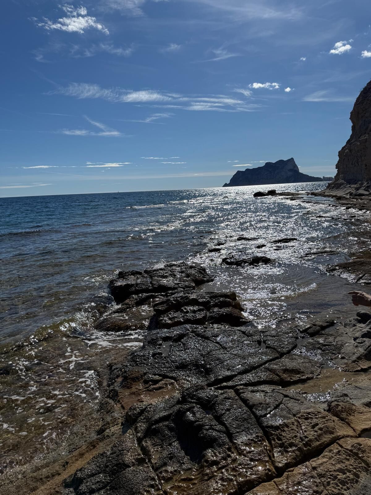 A rocky shoreline with clear water and a distant mountain.