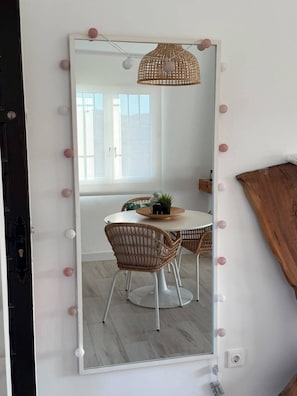 Ein Zimmer mit einem großen Spiegel, Korbstühlen, einem runden Tisch und einer Hängeleuchte.