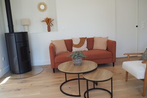 A living room with a sofa, two round tables, a potted plant, a fireplace, and a mirror on the wall.