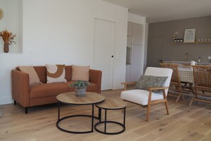 Ein Wohnzimmer mit Sofa, Sessel und Couchtisch, ein Essbereich mit Tisch und Stühlen sowie eine Küche im Hintergrund.