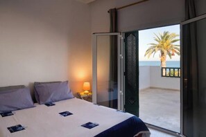A hotel room with a bed, a nightstand with a lamp, a sliding glass door leading to a balcony with a palm tree view. - Vrbo Property (Tunis Governorate)