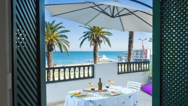 Ein Balkon mit Esstisch, der auf einen Strand mit Palmen und das Meer blickt.