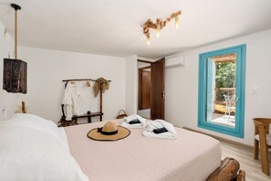 Um quarto com cama, chapéu, toalhas, cabeceira de madeira, luminária pendente e janela com vista.