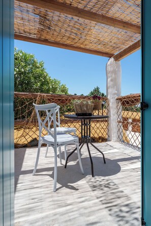 Een overdekt terras met een tafel, stoelen, een rieten mand en uitzicht op het omliggende landschap.