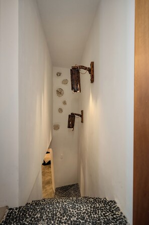 Een smalle gang met een patroon vloer, een houten deur en een wandlamp.