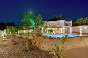 Um edifício de dois andares com piscina, paredes de pedra e plantas verdes.