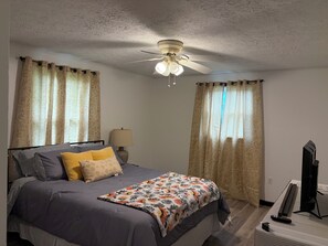 A bedroom with a bed, curtains, a ceiling fan, a lamp, and a television. - Fabulous 3-bedroom house with AC in charming Union (Union)