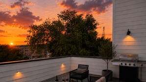 Eine Dachterrasse mit Grill, Sitzgelegenheiten und Blick auf den Sonnenuntergang.