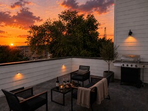 Um terraço no telhado com churrasqueira, área de estar e vista para o pôr do sol.