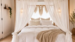 Ein Bett mit Baldachin, ein Zimmerpflanze auf dem Nachttisch und eine Wandleuchte.