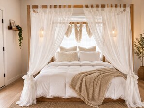 Ein Bett mit Baldachin, ein Zimmerpflanze auf dem Nachttisch und eine Wandleuchte.