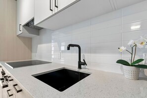 A modern kitchen with white tiles, a black sink, and a potted orchid.