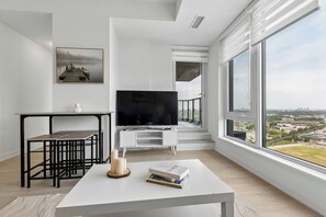 Una sala de estar moderna con un ventanal grande, un televisor de pantalla plana, una mesa de comedor y una estantería.