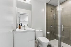 Un baño moderno con cabina de ducha de vidrio, un lavabo blanco y un inodoro.
