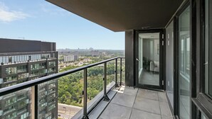 A balcony with a glass door leading to an interior space, a metal railing, and a view of urban buildings and greenery. - Stylish 2bed2bath| Parking | Gym | Sauna|4ppl (Toronto)