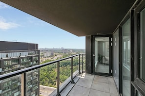 A balcony with a glass door leading to an interior space, a metal railing, and a view of urban buildings and greenery.