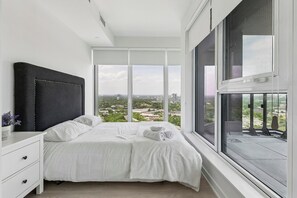 Un dormitorio con una ventana grande, una cama, una mesita de noche y vistas a la ciudad.