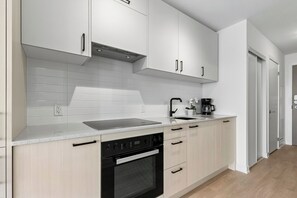 Una cocina moderna con armarios blancos, una campana extractora de acero inoxidable, un horno empotrado y una encimera con cafetera.