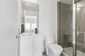 A modern bathroom with a white sink, mirror, toilet, and glass-enclosed shower.