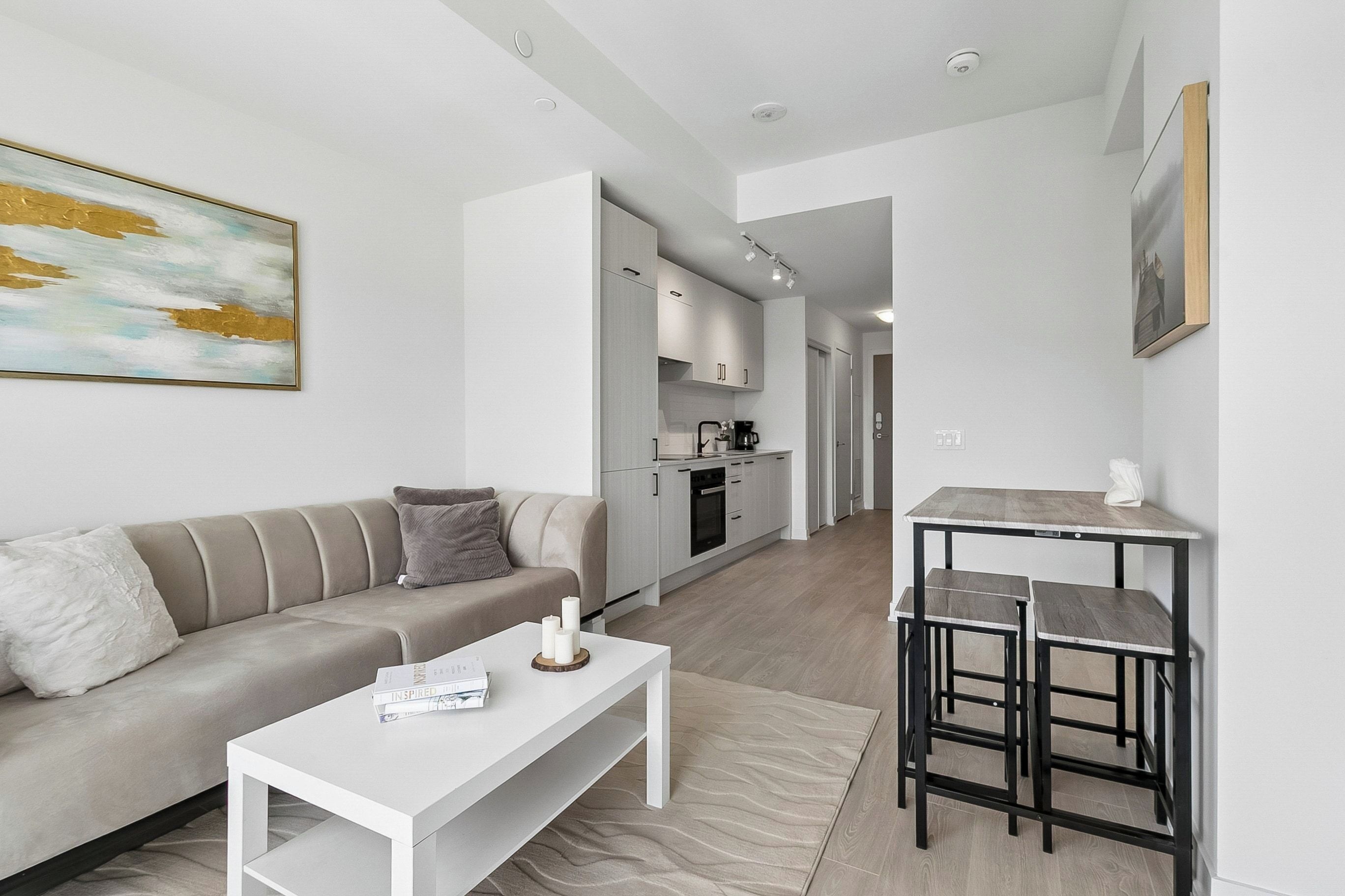 A modern living room with a sofa, coffee table, and a dining area with bar stools.