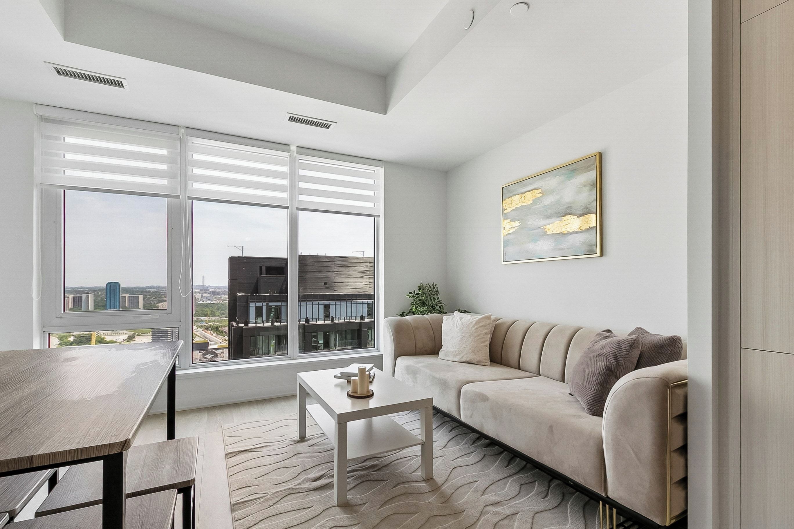 Un salon moderne avec un canapé, une table basse et une vue sur la ville grâce à de grandes fenêtres.