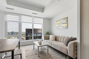 A modern living room with a sofa, coffee table, and a view of the city through large windows.