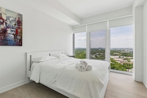 A modern bedroom with a large bed, a city view, and a painting on the wall.