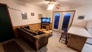 Un espacio habitable compacto con sofá, una mesita, televisor y una zona de kitchenette.