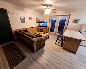 Un espacio habitable compacto con sofá, una mesita, televisor y una zona de kitchenette.