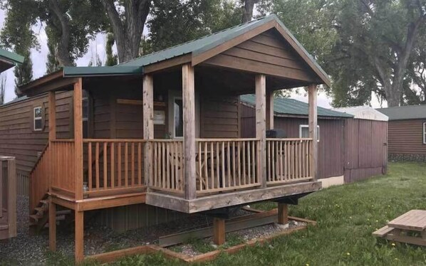 A wooden cabin with a porch, a small staircase, and a fenced yard.