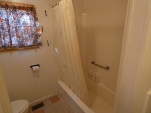 Un baño con ducha, inodoro y una ventana con cortinas estampadas.