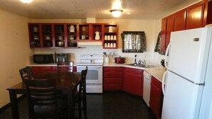Cocina compacta con mesa, sillas, microondas, estufa, refrigerador y armarios.