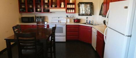A compact kitchen with a dining table, chairs, a microwave, stove, refrigerator, and cabinets.