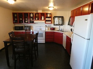 Cocina compacta con mesa, sillas, microondas, estufa, refrigerador y armarios.