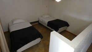 Un alojamiento pequeño de una sola habitación con dos camas, una lámpara en el techo y suelo de baldosas.
