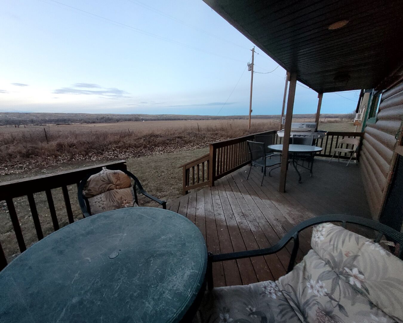 A covered outdoor deck with a table and chairs, overlooking a flat landscape.