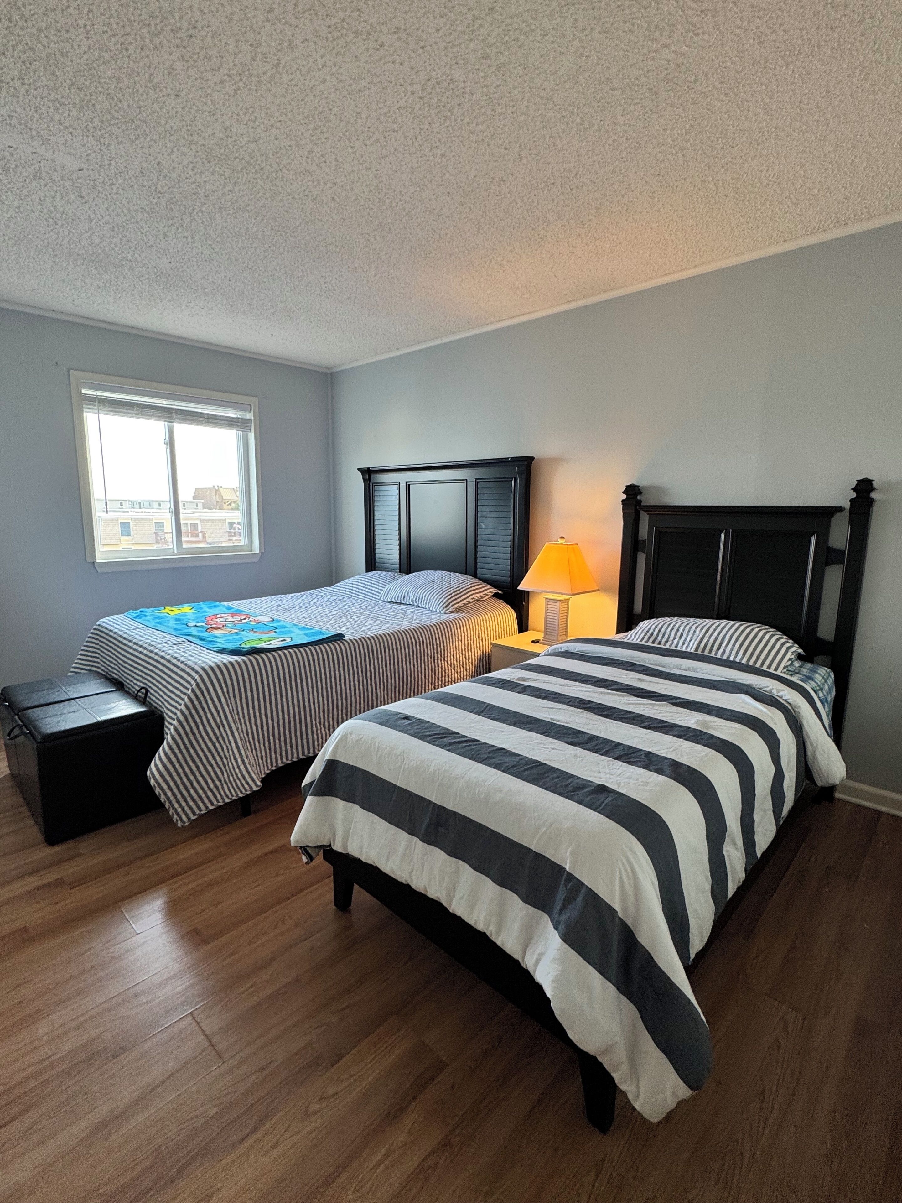 A bedroom with two beds, a window, a nightstand, and a lamp.