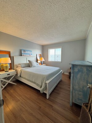 Une chambre à coucher avec un lit, des tables de chevet, une commode, une fenêtre et un plafond.